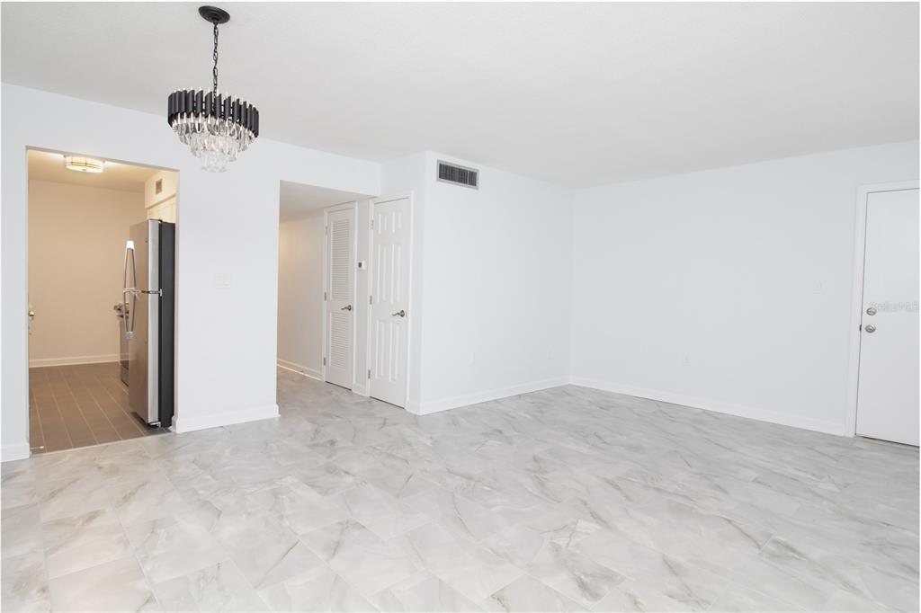 A bright room with white walls, marble-look tile flooring, and a modern crystal chandelier — 1115 RUE DES CHATEAUX UNIT 1A, SOUTH PASADENA, FL