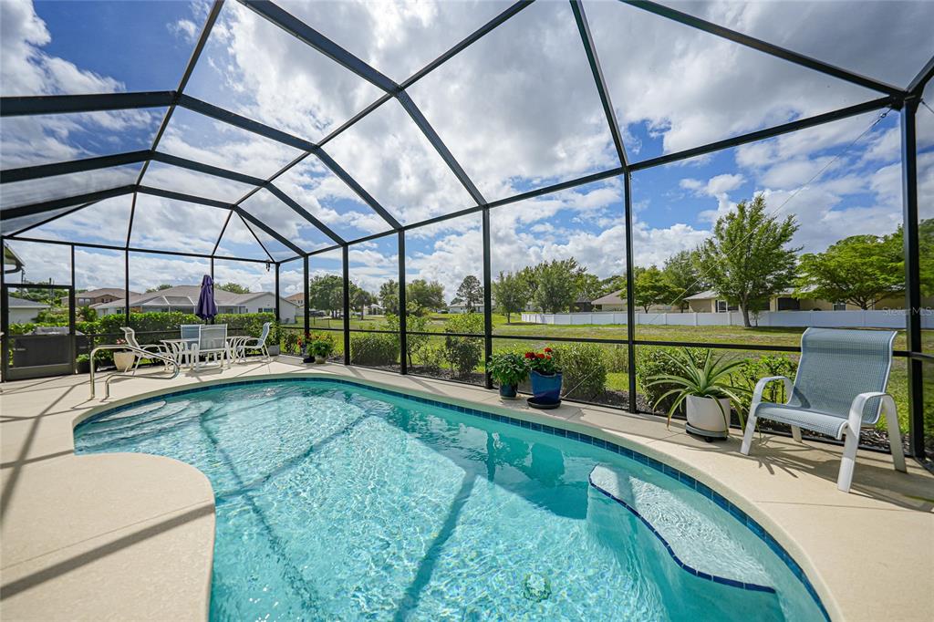 A screened-in pool patio features a kidney-shaped swimming pool and outdoor furniture — 25091 PALISADE ROAD, PUNTA GORDA, FL