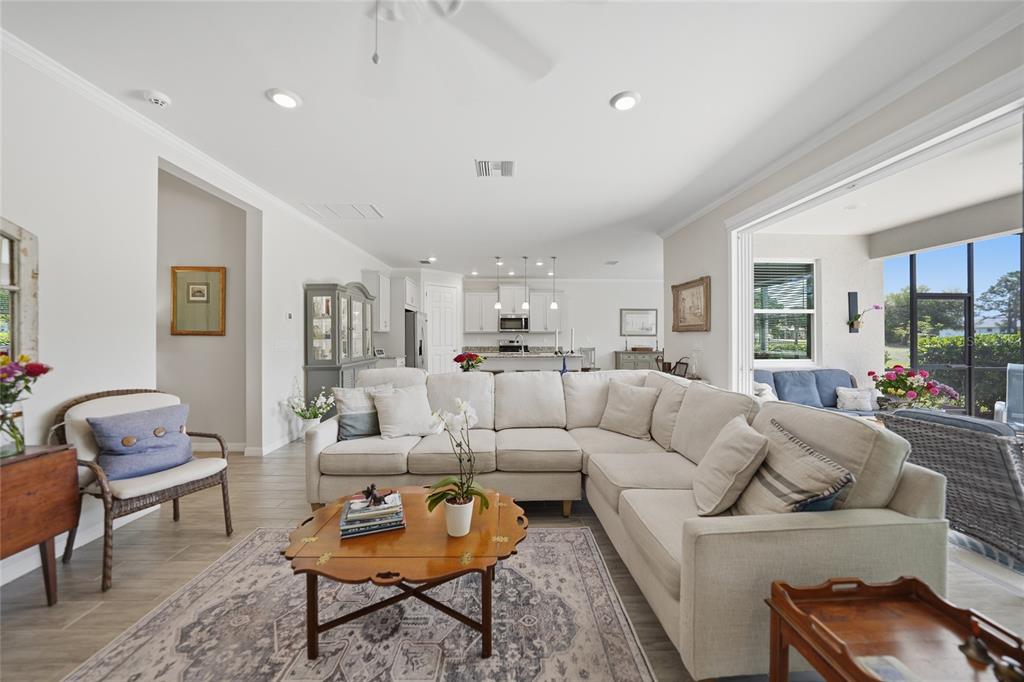 A bright, open-concept living room features a large sectional sofa, area rug, and kitchen beyond — 25091 PALISADE ROAD, PUNTA GORDA, FL