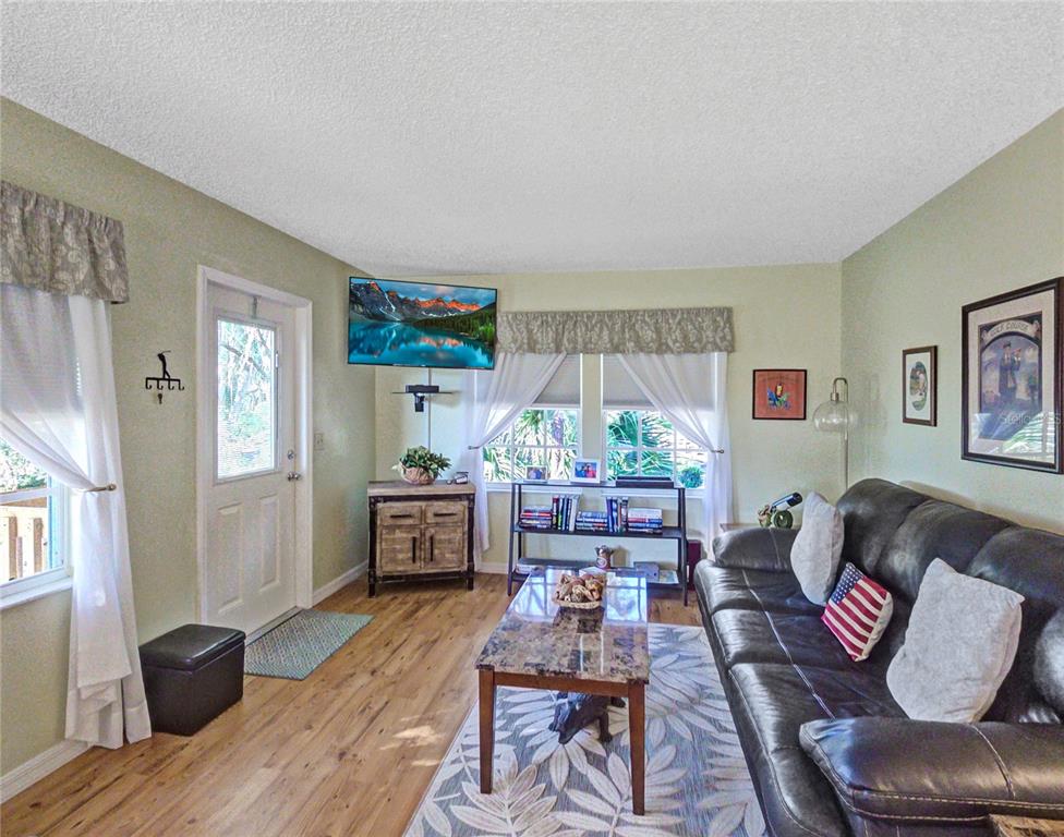 A living room with a dark leather sofa, a coffee table, and a wall-mounted television — 7991 MIDWAY DRIVE TERRACE UNIT L201, OCALA, FL
