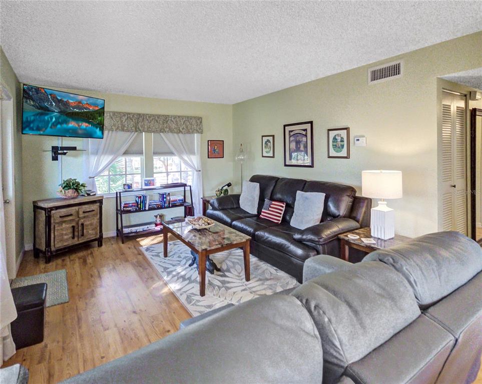 A living room features a dark leather sofa, a coffee table, and a wall-mounted television — 7991 MIDWAY DRIVE TERRACE UNIT L201, OCALA, FL