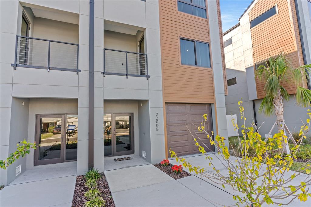 A modern two-story townhouse exterior features a garage, glass entry doors, and upper-level balconies — 2200 BAY BOULEVARD UNIT B, INDIAN ROCKS BEACH, FL