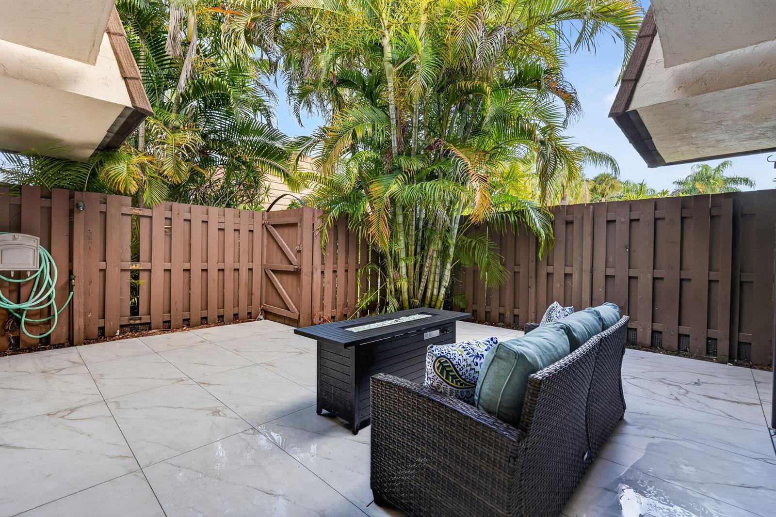 A patio features light-colored tile flooring, a wicker sofa, a fire pit, and a wooden fence — 825 Center Street # 32b, Jupiter FL 33458, JUPITER, FL