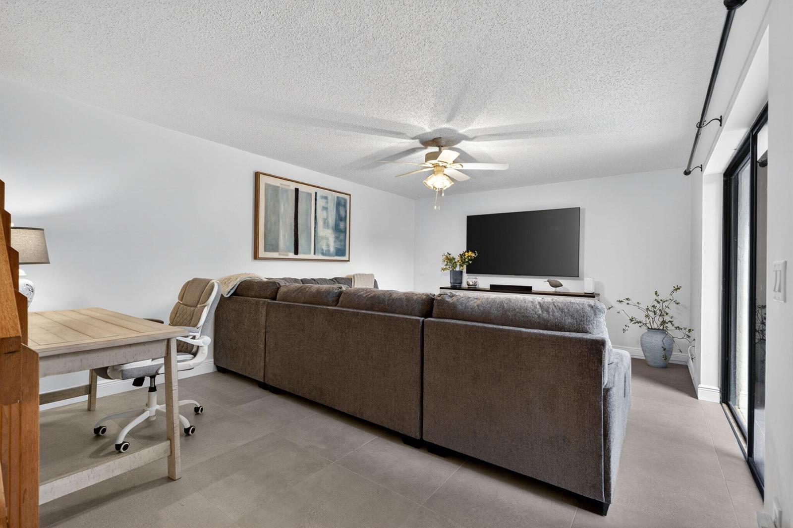 A living room features a large gray sectional sofa, a desk, and a wall-mounted television — 825 Center Street # 32b, Jupiter FL 33458, JUPITER, FL