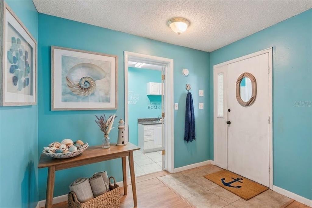 A bright turquoise entryway features a wooden console table, coastal decor, and a white door — 905 VAN DRIVE, AUBURNDALE, FL
