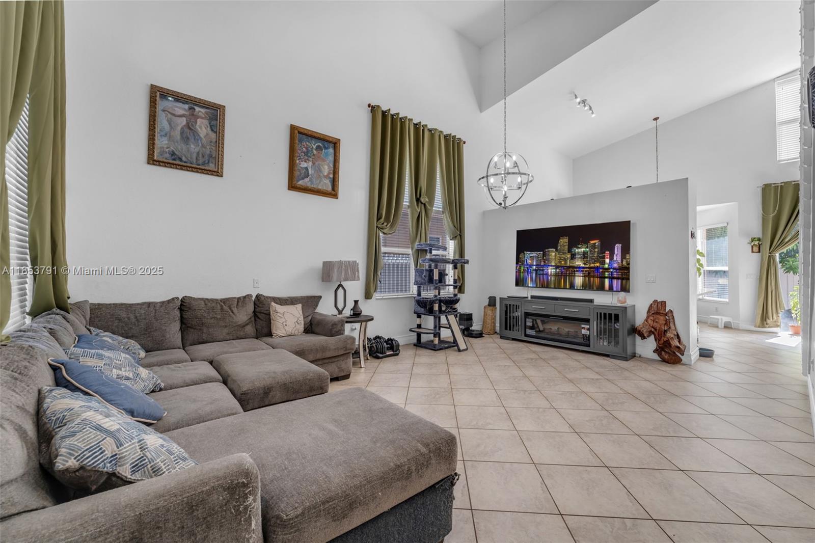 A spacious living room features high ceilings, tile flooring, a large sectional sofa, and a television — 1755 NE 37th Ave # 0, Homestead FL 33033, HOMESTEAD, FL