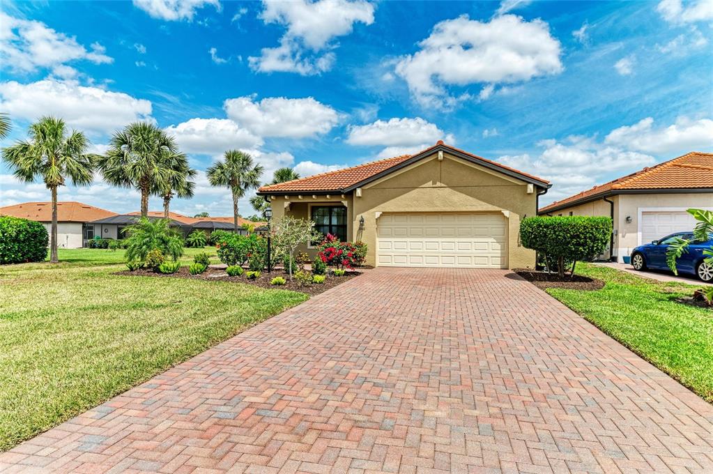 A single-story house with a tan stucco exterior, tile roof, and a brick paver driveway — 10111 MALACHITE DRIVE, BRADENTON, FL