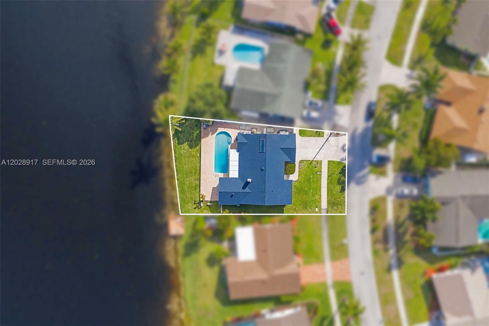 An aerial view shows a house with a swimming pool situated next to a lake — 1310 SW 26th Ave, Deerfield Beach FL 33442, DEERFIELD BEACH, FL