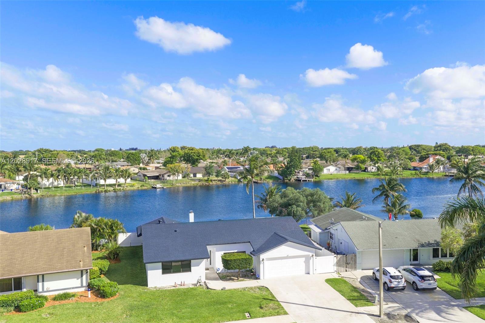 An aerial view shows a white house with a dark roof beside a lake — 1310 SW 26th Ave, Deerfield Beach FL 33442, DEERFIELD BEACH, FL