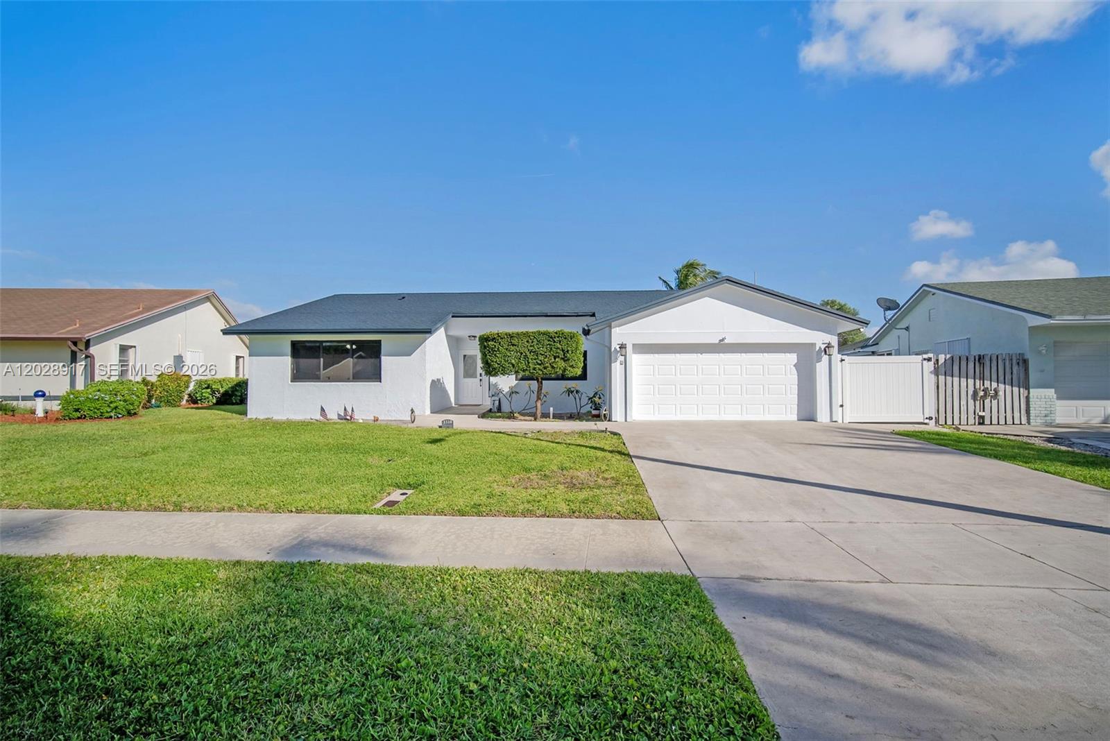 A white single-story house with a dark roof, a two-car garage, and a front lawn — 1310 SW 26th Ave, Deerfield Beach FL 33442, DEERFIELD BEACH, FL