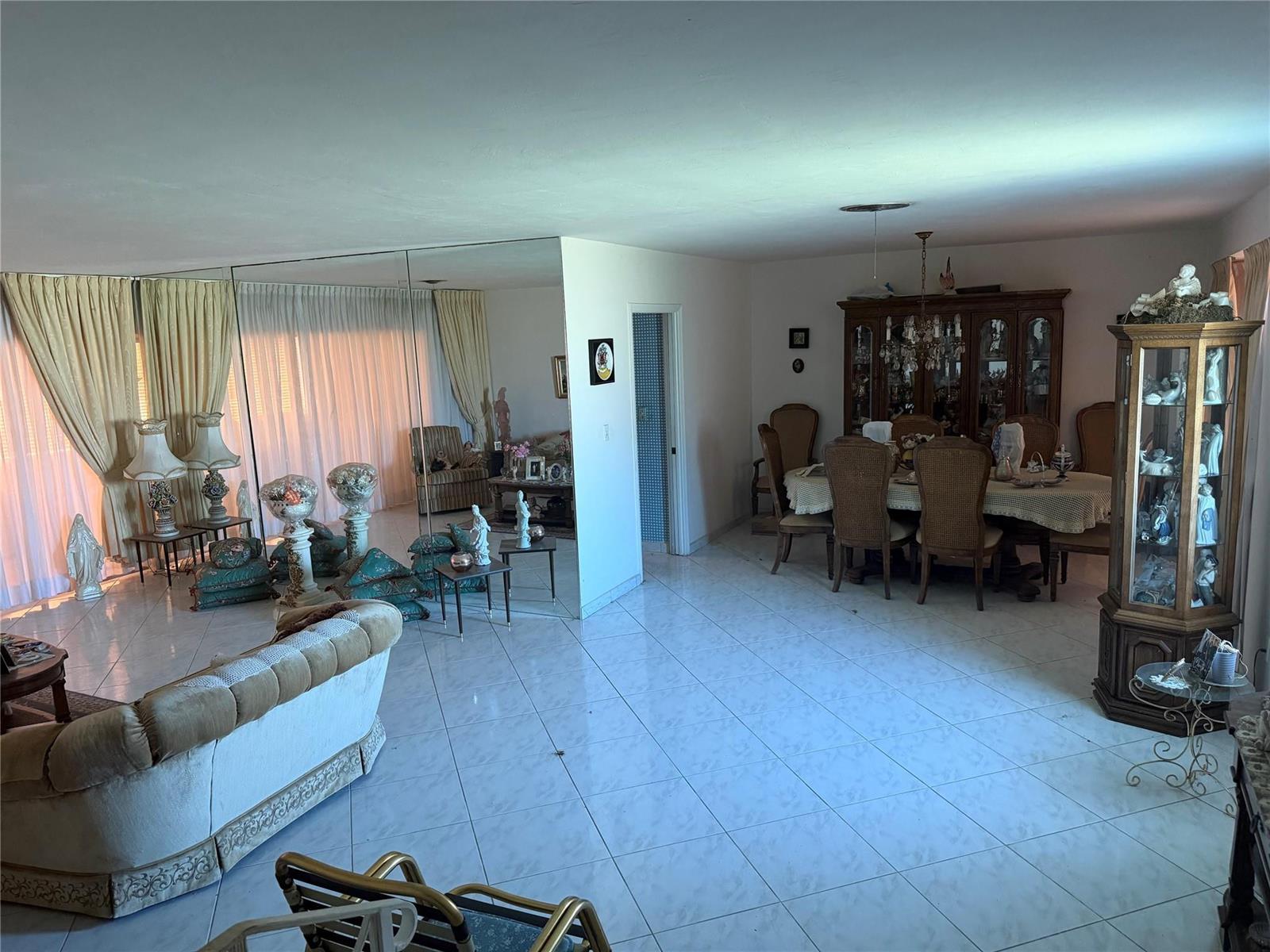 A spacious living and dining room features white tile flooring, mirrored walls, and traditional furniture — 8230 SW 87th Terrace, Miami FL 33143, MIAMI, FL