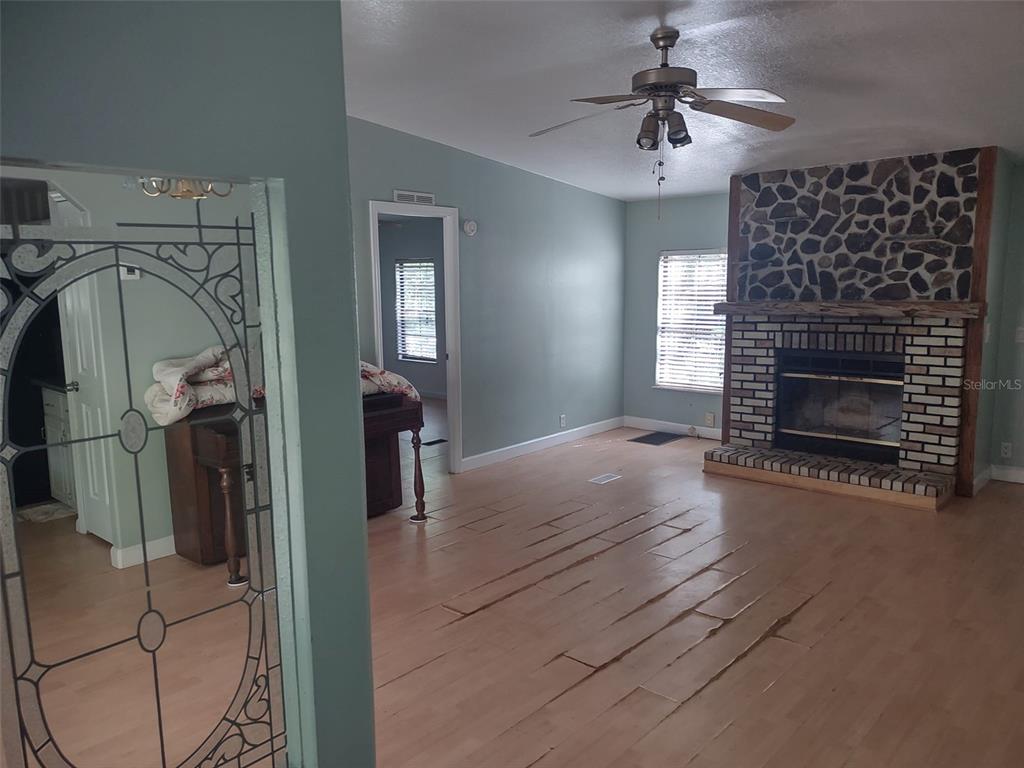 A living room features light wood flooring, a stone fireplace, and a ceiling fan — 56508 BLUE CREEK ROAD, ASTOR, FL