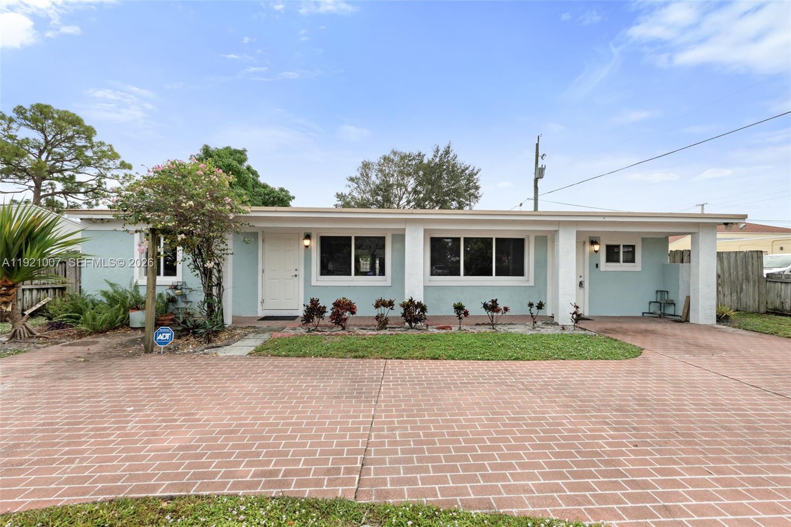A light blue, single-story house features a brick driveway, a covered porch, and landscaping — 112 Milton St # 114, Lantana FL 33462, LANTANA, FL