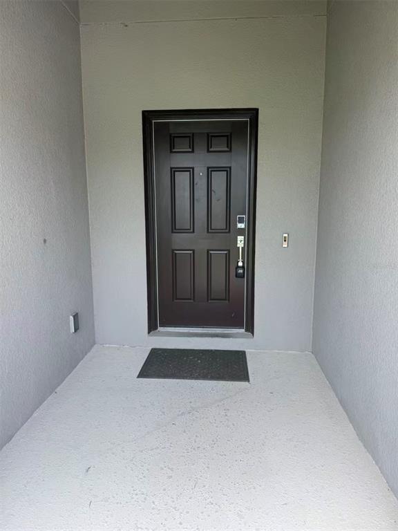 A dark brown front door is centered in a small, covered concrete entryway — 16493 CHAMPLAIN STREET, CLERMONT, FL
