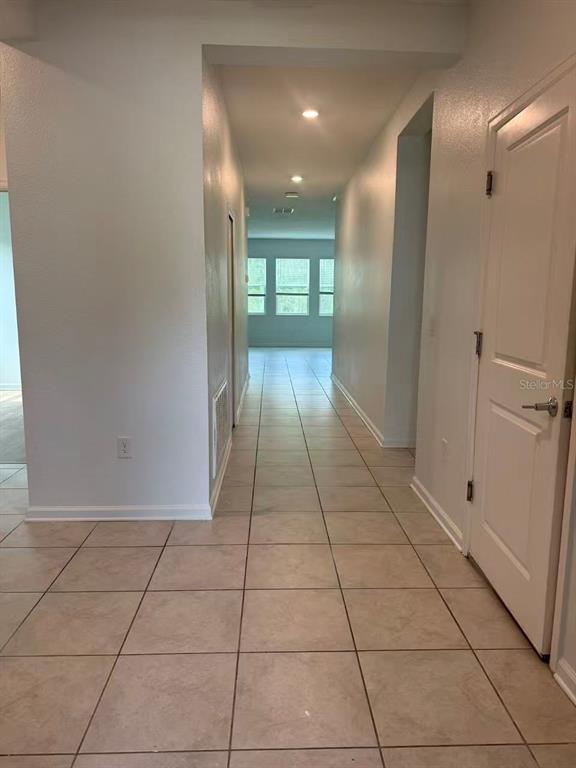 A hallway with light-colored tile flooring leads toward a windowed room in the distance — 16493 CHAMPLAIN STREET, CLERMONT, FL
