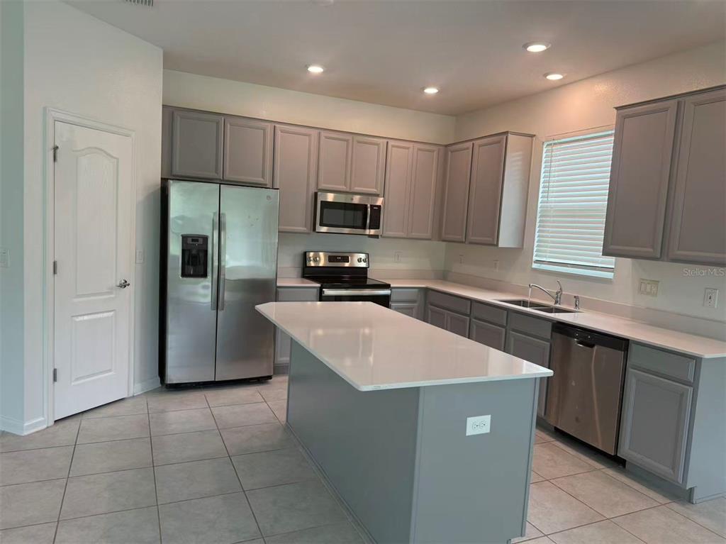 A kitchen features gray cabinets, stainless steel appliances, a white island, and tile flooring — 16493 CHAMPLAIN STREET, CLERMONT, FL