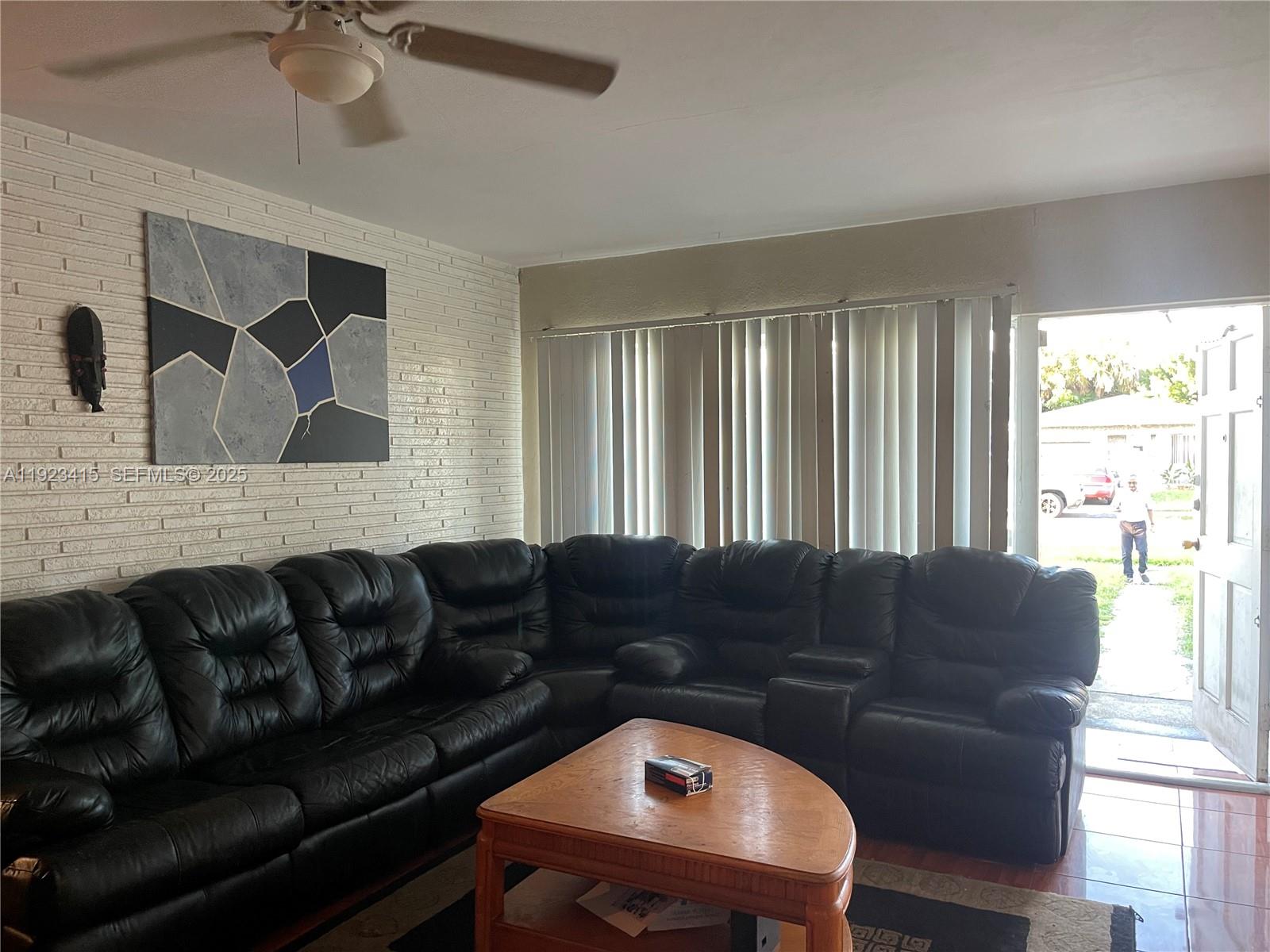A living room features a large black sectional sofa, a brick wall, and a doorway — 3880 NW 6th St, Lauderhill FL 33311, LAUDERHILL, FL
