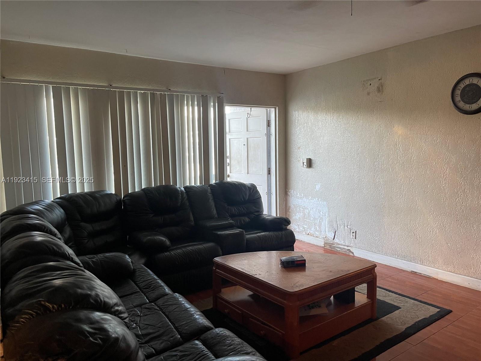 A living room features a black leather sectional, a wooden coffee table, and a wall clock — 3880 NW 6th St, Lauderhill FL 33311, LAUDERHILL, FL
