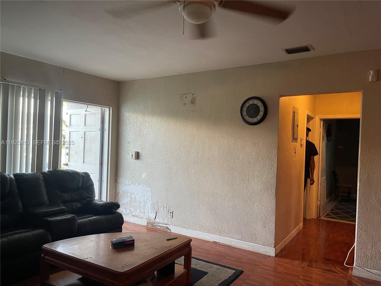 A living room features a black leather sofa, a wooden coffee table, and damaged wall plaster — 3880 NW 6th St, Lauderhill FL 33311, LAUDERHILL, FL