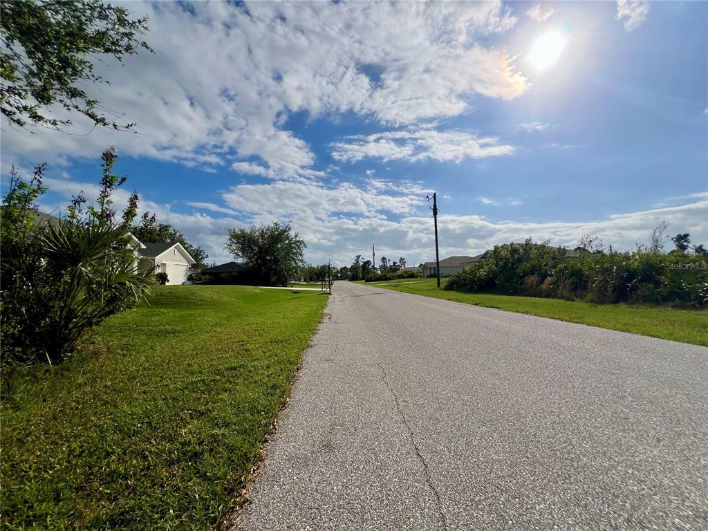 A paved suburban street stretches toward the horizon under a bright, partly cloudy sky — 4396 SINES LANE, PORT CHARLOTTE, FL