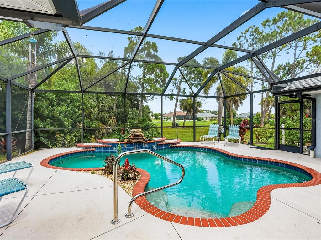 A screened-in swimming pool with a rock waterfall feature and patio furniture — 61 PINE VALLEY COURT, ROTONDA WEST, FL