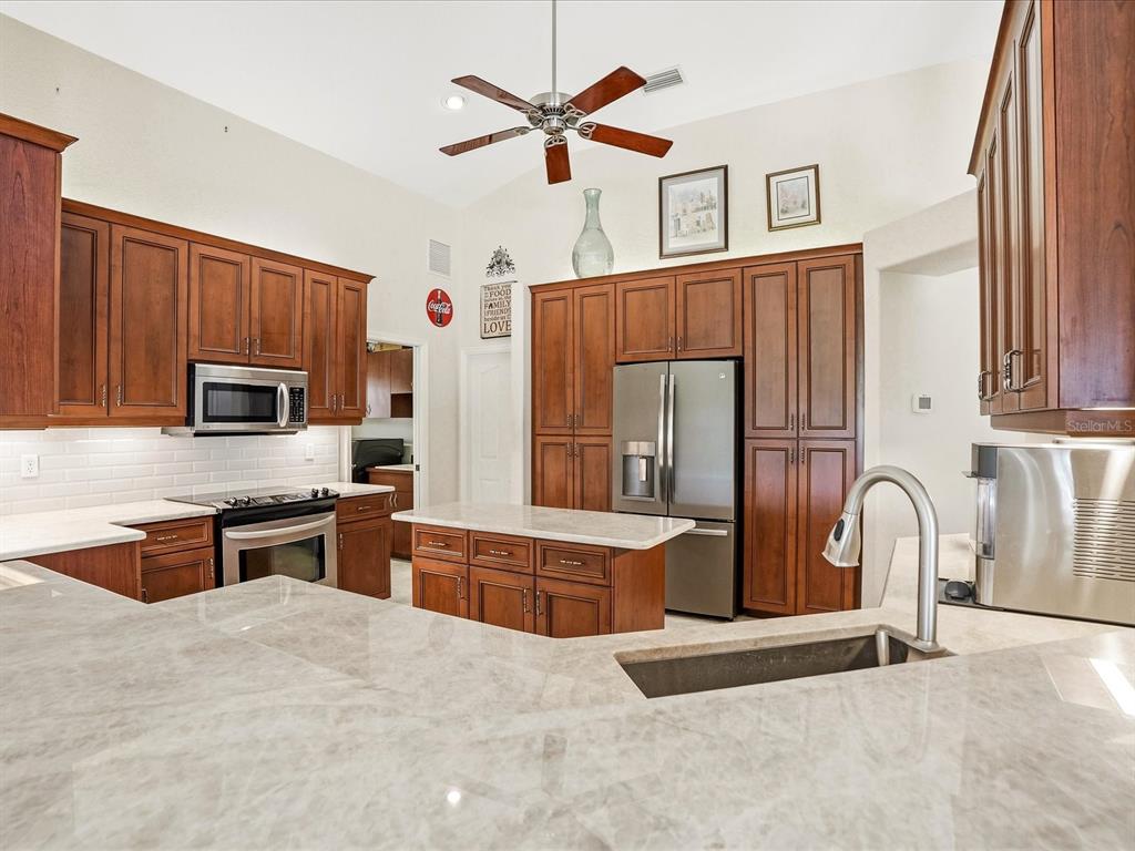 A kitchen features wood cabinets, stainless steel appliances, a center island, and light stone countertops — 61 PINE VALLEY COURT, ROTONDA WEST, FL