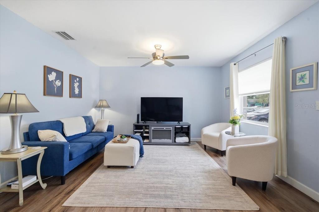 A living room features a blue sofa, two white chairs, and a television on a stand — 12291 MALLORY DRIVE, LARGO, FL