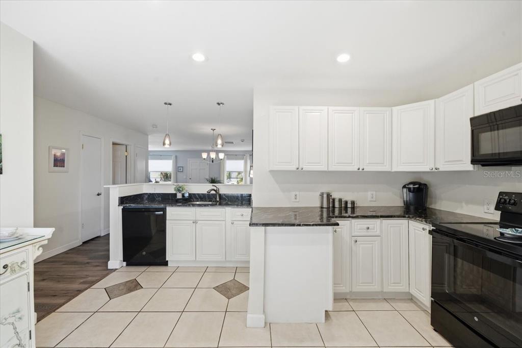 A kitchen features white cabinets, black countertops, and light-colored tile flooring — 12291 MALLORY DRIVE, LARGO, FL