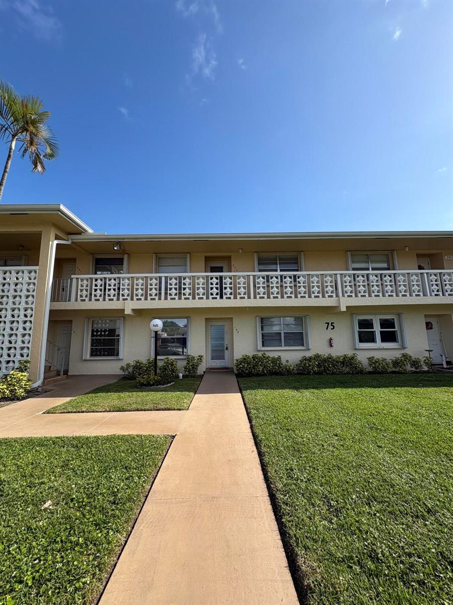 A two-story apartment building exterior features a concrete walkway, green lawn, and a balcony — 1421 NW 19th Terrace # 202, Delray Beach FL 33445, DELRAY BEACH, FL