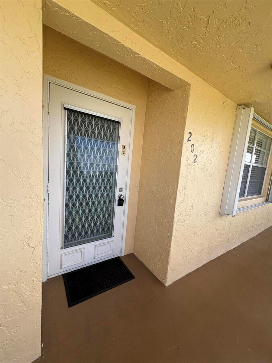 A white front door with a decorative glass insert is labeled with the number 202 — 1421 NW 19th Terrace # 202, Delray Beach FL 33445, DELRAY BEACH, FL