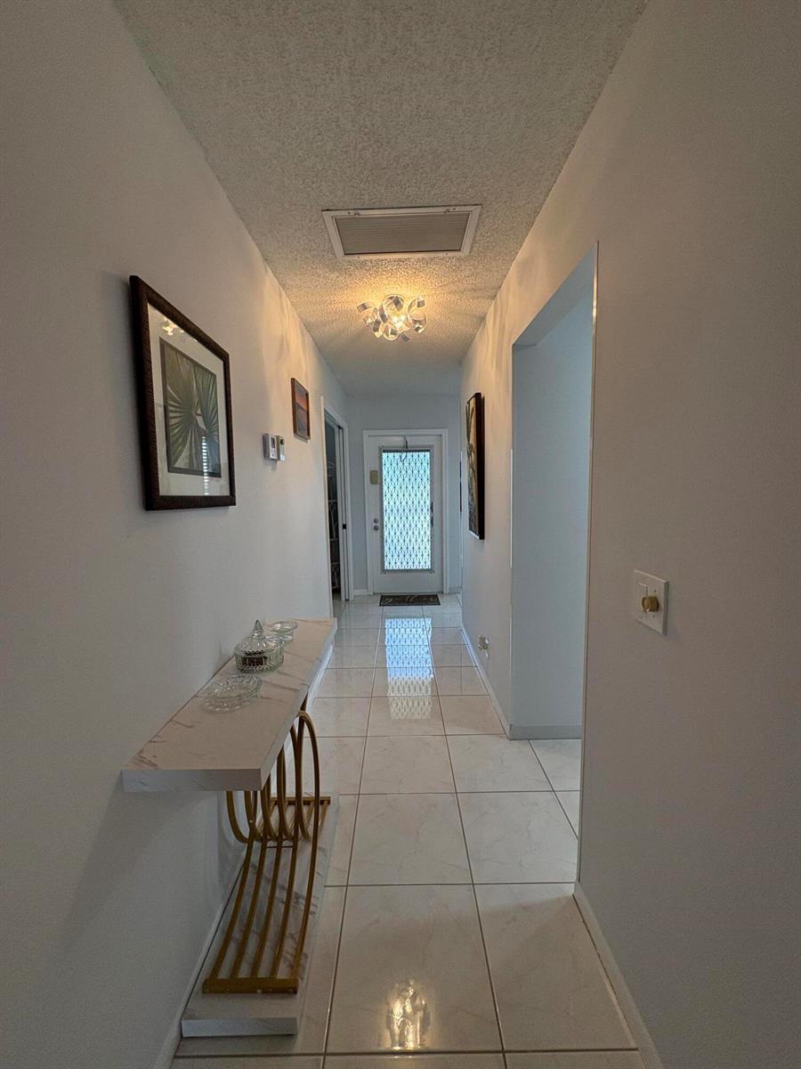 A hallway features white tile floors, a marble-topped console table, and a modern ceiling light — 1421 NW 19th Terrace # 202, Delray Beach FL 33445, DELRAY BEACH, FL