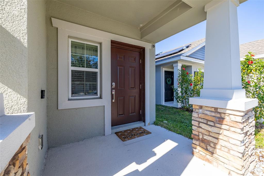 A covered front porch features a brown door, a window, and stone-accented columns — 1066 BERRY LANE, DAVENPORT, FL