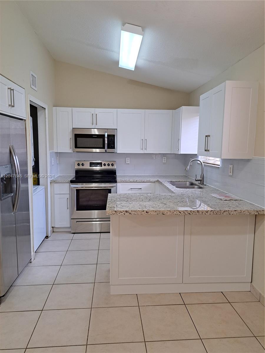 A kitchen features white cabinets, granite countertops, stainless steel appliances, and light-colored tile flooring — 17318 NW 74th Ave # 202, Hialeah FL 33015, HIALEAH, FL