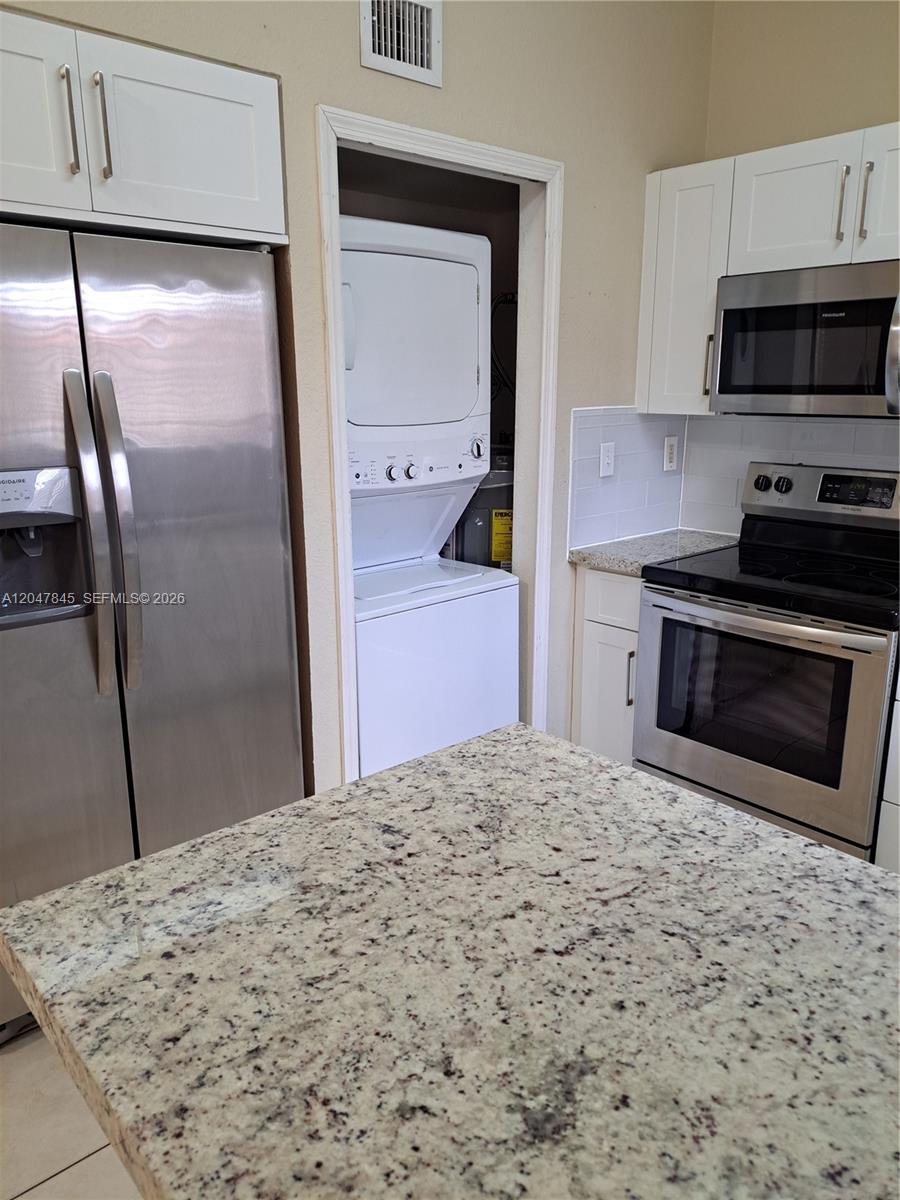 A kitchen features stainless steel appliances, white cabinets, granite countertops, and a stacked laundry unit — 17318 NW 74th Ave # 202, Hialeah FL 33015, HIALEAH, FL