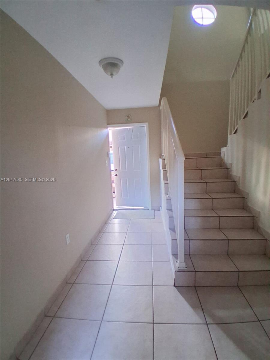 An entryway features light-colored floor tiles, a white front door, and a staircase — 17318 NW 74th Ave # 202, Hialeah FL 33015, HIALEAH, FL