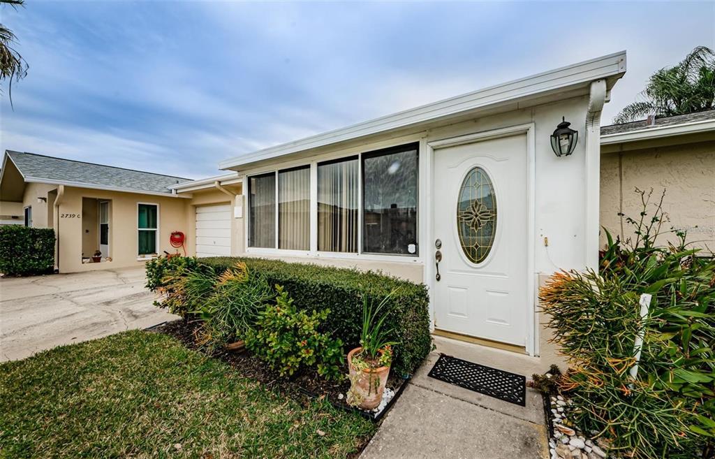 The exterior of a single-story home features a white front door and large windows — 2739 SHERBROOKE LANE UNIT B, PALM HARBOR, FL