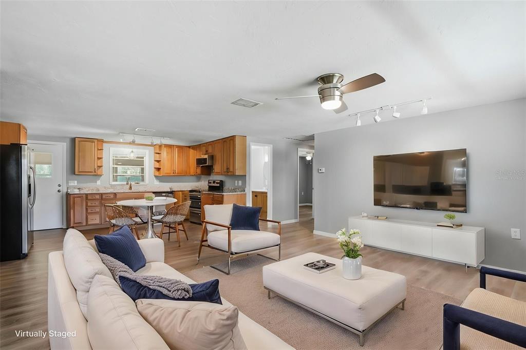 A living room with light wood floors, a large television, and an open-concept kitchen — 8317 LIMAN DRIVE, NEW PORT RICHEY, FL