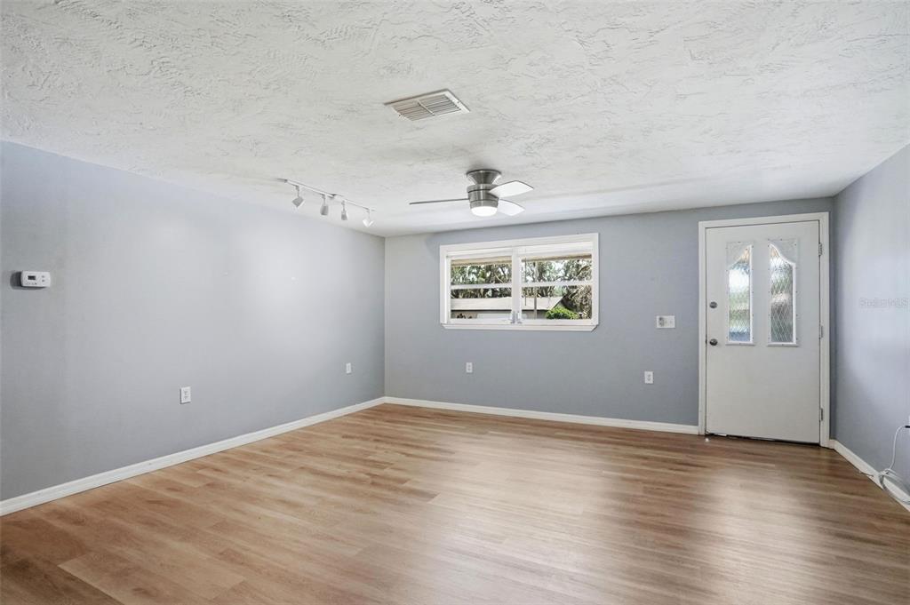An empty room with light gray walls, wood-look flooring, a ceiling fan, and a front door — 8317 LIMAN DRIVE, NEW PORT RICHEY, FL