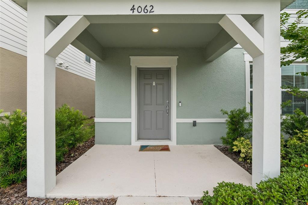 A covered front porch features a gray door, a welcome mat, and white support columns — 4062 FEATHER TREE DRIVE, APOPKA, FL