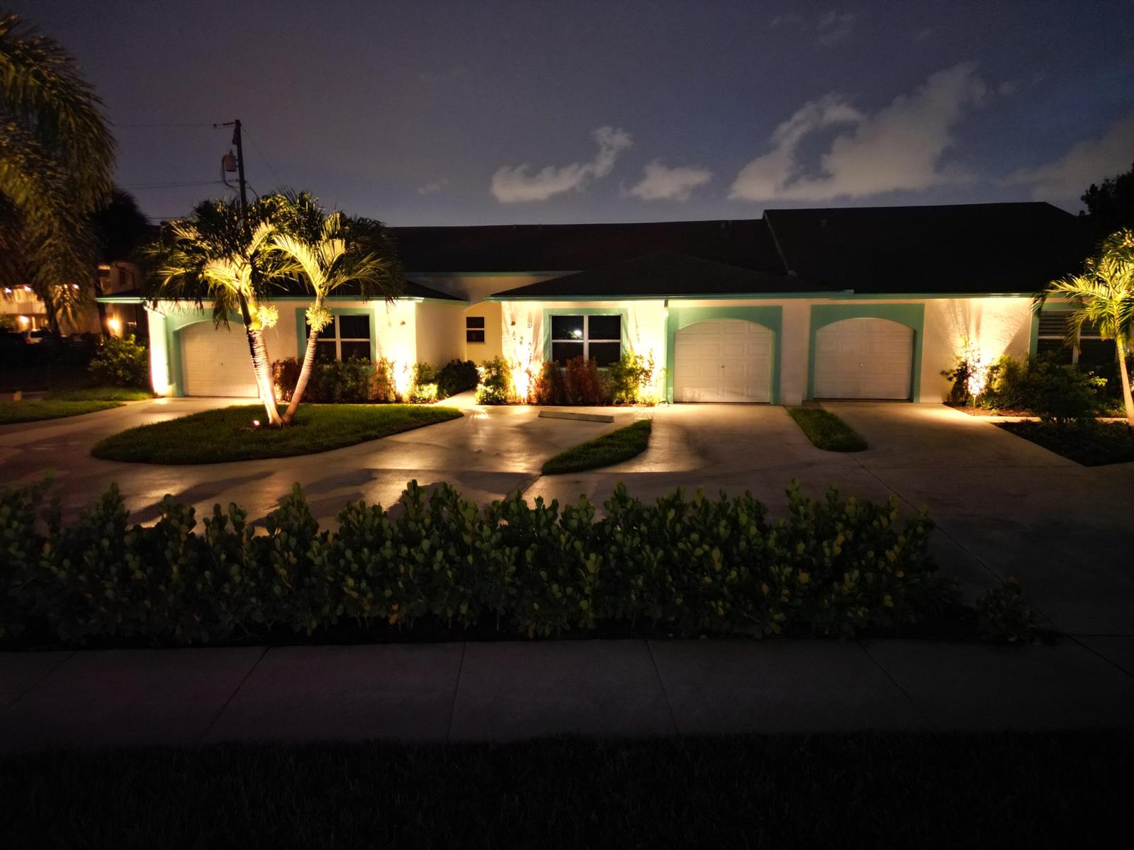 A single-story house with three garage bays and illuminated landscaping at night — 620 Southwind Circle # A, North Palm Beach FL 33408, NORTH PALM BEACH, FL