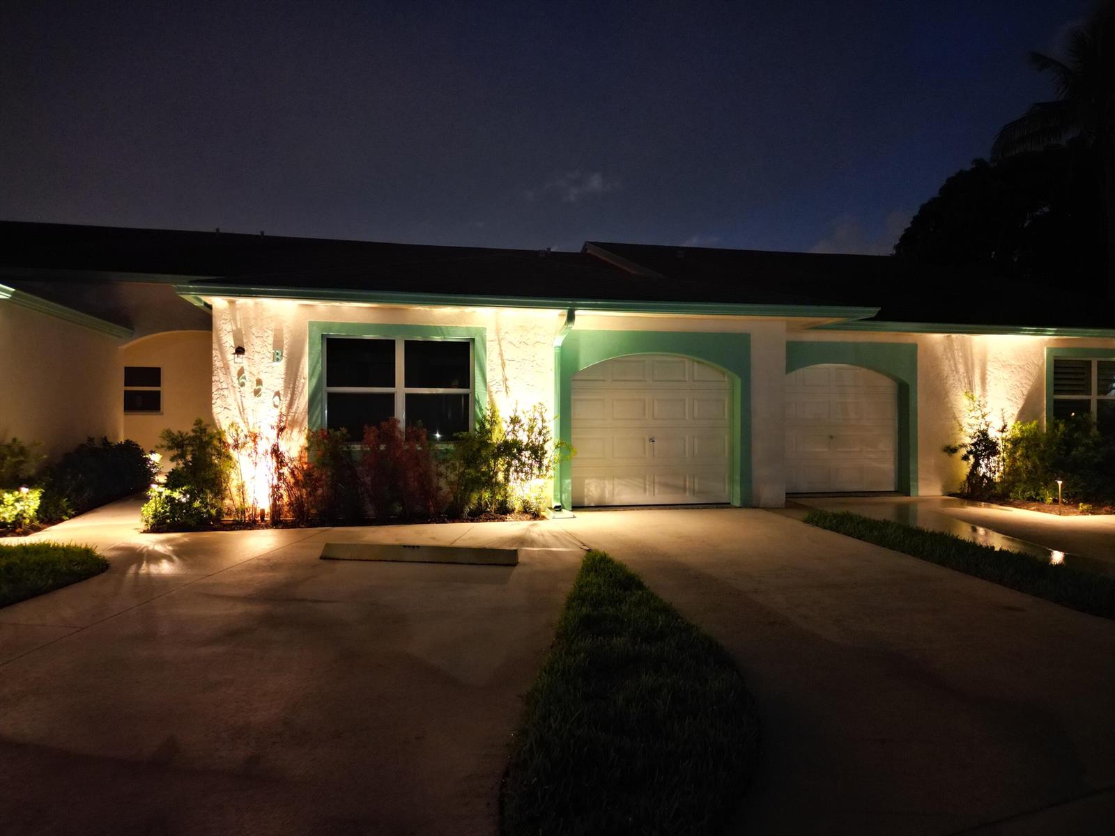 A house exterior at night with illuminated landscaping, a two-car garage, and teal trim — 620 Southwind Circle # A, North Palm Beach FL 33408, NORTH PALM BEACH, FL