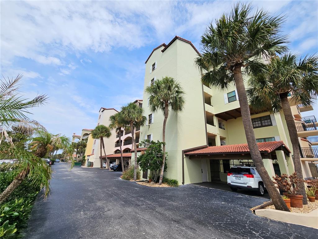 A multi-story pale yellow apartment building with palm trees and a covered parking area — 632 MARINA POINT DRIVE UNIT 6320, DAYTONA BEACH, FL