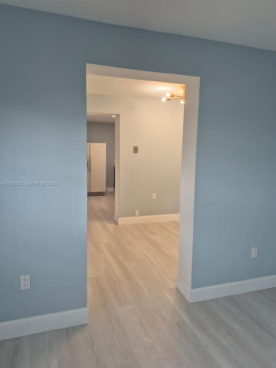 A view through a doorway shows a kitchen with light wood flooring and blue walls — 1231 NW 101st St # 2, Miami FL 33147, MIAMI, FL