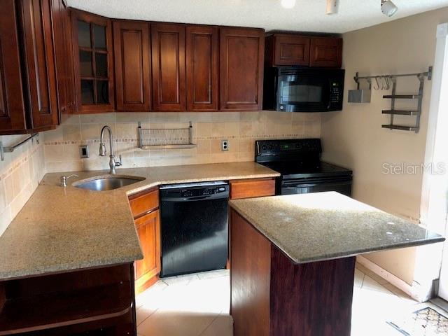 A kitchen features dark wood cabinets, granite countertops, a black dishwasher, and a small island — 3222 ACACIA STREET, LUTZ, FL