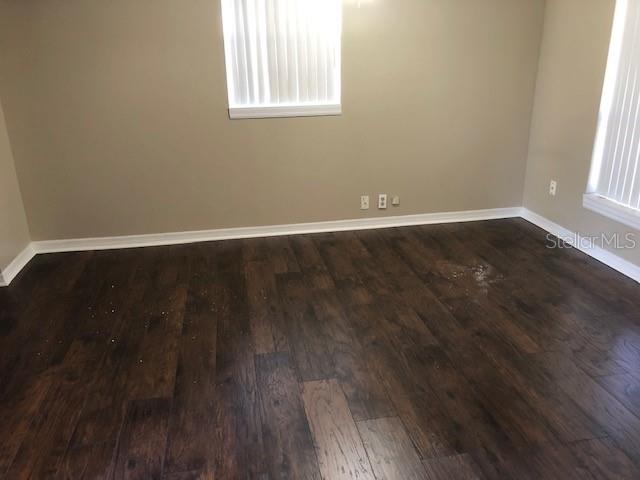 An empty room features dark wood-look flooring, beige walls, and two windows with vertical blinds — 3222 ACACIA STREET, LUTZ, FL