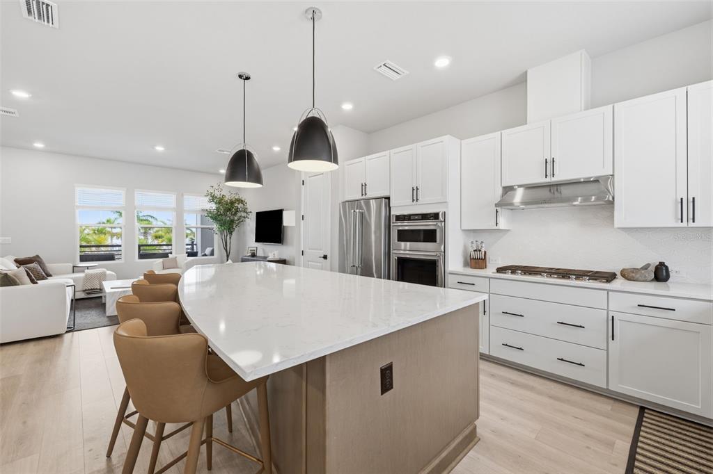 A modern kitchen features a large white quartz island, light wood cabinetry, and stainless appliances — 1528 SKYSAIL LANE, SARASOTA, FL
