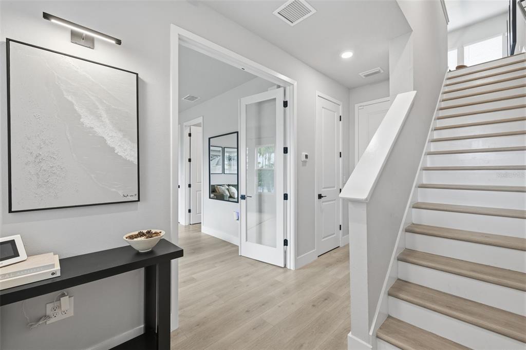 A modern entryway features light wood flooring, a staircase, and a glass-paneled door — 1528 SKYSAIL LANE, SARASOTA, FL