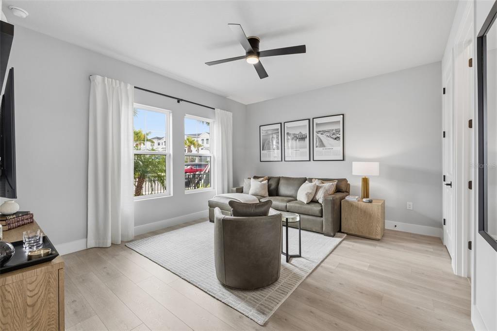 A living room features a gray sofa, a swivel chair, light wood floors, and windows — 1528 SKYSAIL LANE, SARASOTA, FL