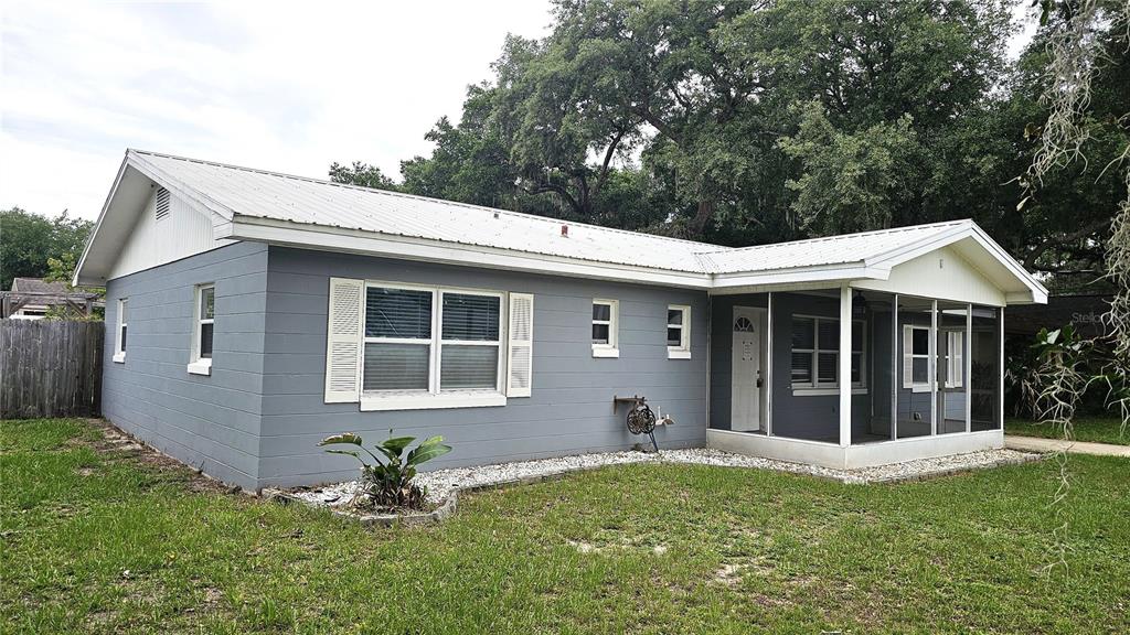 A single-story gray house with a white metal roof and a screened-in front porch — 314 WOODLAND DRIVE, EUSTIS, FL