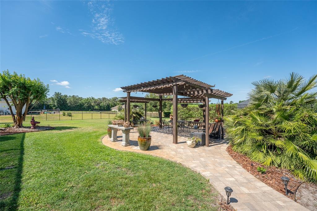 A backyard features a wooden pergola over a paved patio with outdoor seating and landscaping — 7830 SE 25TH AVENUE, OCALA, FL